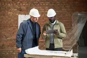 African American designer of interior showing layout plan of IT office on tablet to Caucasian foreman dressed in uniform
