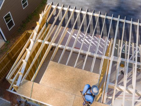 In course of construction work, carpenter hammers nails into OSB plywood panels that are mounted on roof