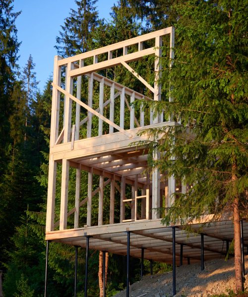 Housing wooden-frame house being erected close to forested area. Start of new construction project for cozy house. Concept of contemporary ecological construction and modern architectural design.